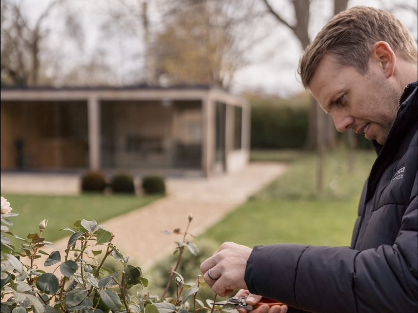 Man pruning hedge in a large garden.
